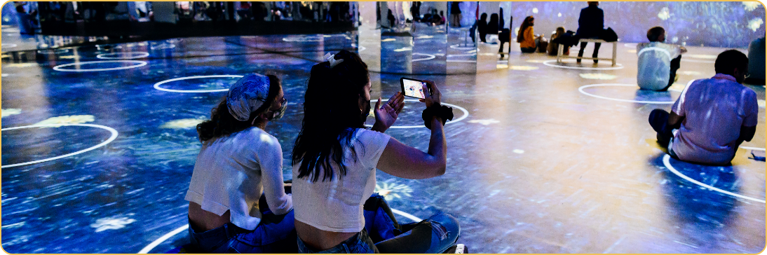 Visitors seated on a projected starry floor inside the exhibit